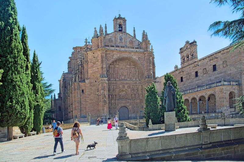 DC 22-0794-049.jpg :: Saga Douro River Cruise, Salamanca. Spain: The image shows the Convent of San Esteban (St. Stephen) in Salamanca. It is a Dominican monastery with a mix of Gothic, Renaissance, and Baroque architectural styles. The most notable feature is the ornate Plateresque facade of the church, which resembles intricate silversmith's work and forms a triumphal arch. The interior contains a magnificent Baroque altarpiece by José de Churriguera. The convent is a repository of significant history. Christopher Columbus is traditionally believed to have stayed at the previous building on the site while seeking support for his voyages from university geographers. It was an important centre for the Dominican fathers who founded the influential School of Salamanca, including Francisco de Vitoria, considered a founding father of international law. The bronze statue in the foreground is a monument to Francisco de Vitoria. Photo taken 01/09/2022
