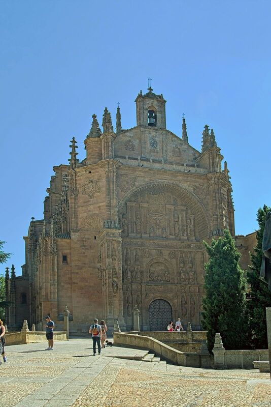 DC 22-0794-050.jpg :: Saga Douro River Cruise, Salamanca. Spain: The image shows the Convent of San Esteban (St. Stephen) in Salamanca. It is a Dominican monastery with a mix of Gothic, Renaissance, and Baroque architectural styles. The most notable feature is the ornate Plateresque facade of the church, which resembles intricate silversmith's work and forms a triumphal arch. The interior contains a magnificent Baroque altarpiece by José de Churriguera. The convent is a repository of significant history. Christopher Columbus is traditionally believed to have stayed at the previous building on the site while seeking support for his voyages from university geographers. It was an important centre for the Dominican fathers who founded the influential School of Salamanca, including Francisco de Vitoria, considered a founding father of international law. The bronze statue in the foreground is a monument to Francisco de Vitoria. Photo taken 01/09/2022