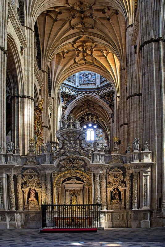 DC 22-0794-084.jpg :: Saga Douro River Cruise, Salamanca. Spain: The ornate interior of the New Cathedral of Salamanca (Catedral Nueva de Salamanca). The cathedral was constructed between the 16th and 18th centuries, resulting in a blend of late Gothic, Renaissance, and Baroque architectural styles. The interior is known for its immense height, with soaring Gothic ribbed vaults that draw the eye heavenward. The image focuses on a highly decorated structure, which is part of the Baroque-style choir or retrochoir, designed by artists including Alberto de Churriguera in the early 18th century. The nave is lined with various side chapels, each with its own unique artistic and architectural details, featuring richly decorated altarpieces and tombs. Medieval and Renaissance stained-glass windows flood the interior with coloured light. Photo taken 01/09/2022