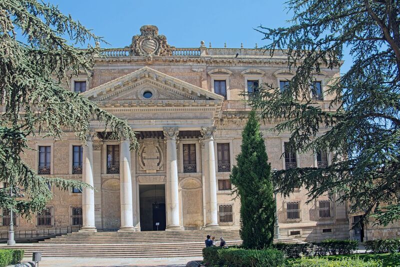 DC 22-0794-086.jpg :: Saga Douro River Cruise, Salamanca. Spain: The Palacio de Anaya, also known as the Colegio Mayor de San Bartolomé. It is located in Salamanca, Spain, and currently houses the Faculty of Philology of the University of Salamanca. The palace is a significant example of Neoclassical architecture, a style that is relatively rare among the predominantly Baroque and Gothic buildings of Salamanca. The original colegio was founded in 1401 by Diego de Anaya Maldonado, Archbishop of Seville. The current building's construction began in 1760, based on plans by José Hermosilla, to replace the previous structure which was badly damaged by the 1755 Lisbon earthquake. The main façade, prominently visible in the image, features a large entranceway with four massive Ionic columns topped by a triangular pediment. The palace is situated in the Plaza de Anaya, a large public square directly opposite the New Cathedral of Salamanca. The area is a hub for university life. Photo taken 01/09/2022