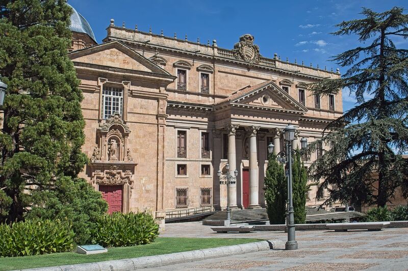 DC 22-0794-088.jpg :: Saga Douro River Cruise, Salamanca. Spain: The Palacio de Anaya, also known as the Colegio Mayor de San Bartolomé. It is located in Salamanca, Spain, and currently houses the Faculty of Philology of the University of Salamanca. The palace is a significant example of Neoclassical architecture, a style that is relatively rare among the predominantly Baroque and Gothic buildings of Salamanca. The original colegio was founded in 1401 by Diego de Anaya Maldonado, Archbishop of Seville. The current building's construction began in 1760, based on plans by José Hermosilla, to replace the previous structure which was badly damaged by the 1755 Lisbon earthquake. The main façade, prominently visible in the image, features a large entranceway with four massive Ionic columns topped by a triangular pediment. The palace is situated in the Plaza de Anaya, a large public square directly opposite the New Cathedral of Salamanca. The area is a hub for university life. Photo taken 01/09/2022