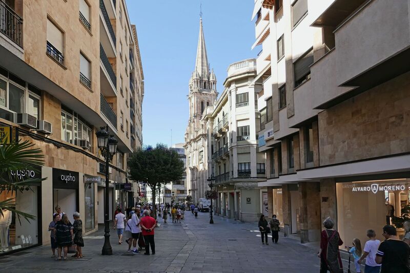 DC 22-0794-093.jpg :: Saga Douro River Cruise, Salamanca. Spain: The street shown in the image is Calle Toro (Toro Street) in the centre of Salamanca, Spain. This bustling street is a main shopping thoroughfare in the city's historic centre. Calle Toro connects the famous Plaza Mayor to other areas of the city centre. The prominent spire visible at the end of the street belongs to the church of La Clerecía (Iglesia del Espíritu Santo). Photo taken 01/09/2022