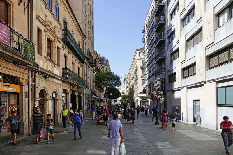 DC 22-0794-099.jpg :: Saga Douro River Cruise, Salamanca. Spain: A bustling street scene in the Spanish city of Salamanca, specifically on Calle Toro. This is the city's main commercial and shopping street, popular with both locals and tourists. The street is in the heart of Salamanca's old centre. It is a pedestrian-friendly street, making it ideal for walking and browsing the shops. The street features a diverse range of shops, including major national brands, smaller local boutiques, opticians, and pharmacies. The street connects directly to the famous Plaza Mayor, one of Spain's most beautiful central plazas. One notable store is a Zara location housed in a converted ancient convent. Photo taken 01/09/2022