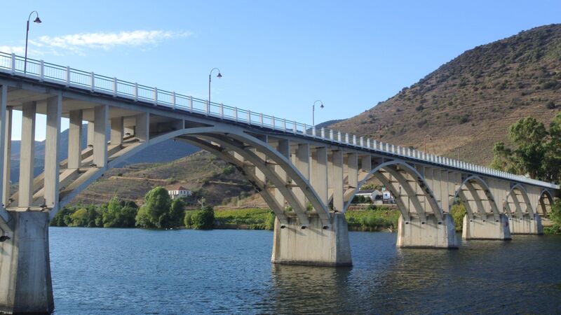 DC 22-0796-001.jpg :: Saga Douro River Cruise, Barca d'Alva, Portugal: Almirante Sarmento Rodrigues Bridge, also known locally as the Barca d'Alva Bridge. It spans the Douro River near the village of Barca d'Alva in Portugal, close to the border with Spain. The bridge is situated in the upper Douro region, specifically near the small village of Barca d'Alva, within the municipality of Freixo de Espada à Cinta, Portugal. It is one of the crossings over the picturesque Douro River, known for its terraced vineyards that produce port wine. The structure is a notable example of modern civil engineering, featuring large, graceful concrete arches supported by substantial pillars emerging from the river. The area around the bridge is part of the Douro International Natural Park and is a popular destination for tourists, including those on Douro River cruises and hikers exploring the region. Photo taken 01/09/2022