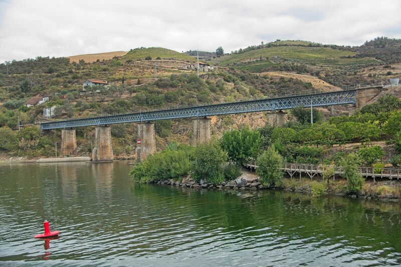 DC 22-0797-021.jpg :: Saga Douro River Cruise, Pocinho to Pinhao, River Douro: The Carrazeda de Ansiães railway bridge (also known as the Foz-Tua bridge) crossing the Douro River in Northern Portugal, a region known for its terraced vineyards. This striking iron truss bridge is located near the confluence of the Tua and Douro rivers in the municipality of Carrazeda de Ansiães. The bridge is situated in the heart of the Alto Douro region, which is a UNESCO World Heritage site known for its Port wine production. It is a railway bridge, part of the historical Douro railway line. The original structure was built in the late 19th or early 20th century, but a new bridge was constructed in 1980, featuring a mix of reinforced concrete for the access structures and a central metal truss. Photo taken 02/09/2022