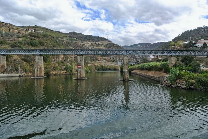 DC 22-0797-022.jpg :: Saga Douro River Cruise, Pocinho to Pinhao, River Douro: The Carrazeda de Ansiães railway bridge (also known as the Foz-Tua bridge) crossing the Douro River in Northern Portugal, a region known for its terraced vineyards. This striking iron truss bridge is located near the confluence of the Tua and Douro rivers in the municipality of Carrazeda de Ansiães. The bridge is situated in the heart of the Alto Douro region, which is a UNESCO World Heritage site known for its Port wine production. It is a railway bridge, part of the historical Douro railway line. The original structure was built in the late 19th or early 20th century, but a new bridge was constructed in 1980, featuring a mix of reinforced concrete for the access structures and a central metal truss. Photo taken 02/09/2022