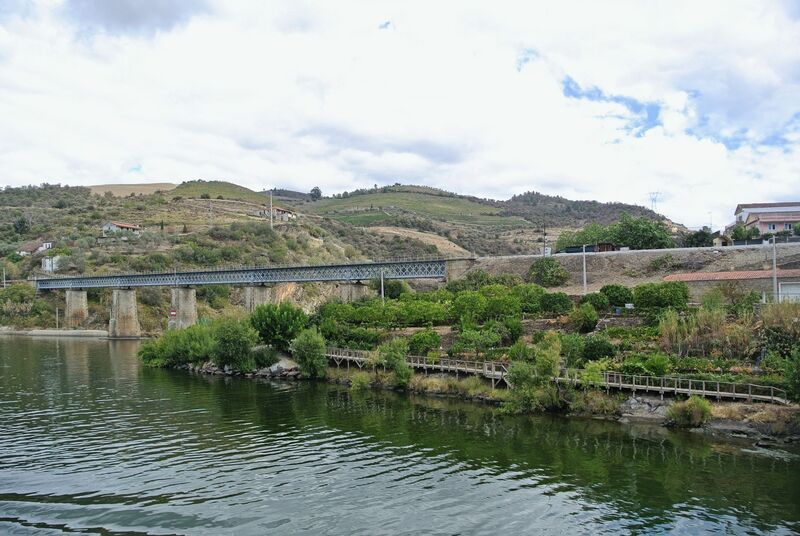 DC 22-0797-023.jpg :: Saga Douro River Cruise, Pocinho to Pinhao, River Douro: The Carrazeda de Ansiães railway bridge (also known as the Foz-Tua bridge) crossing the Douro River in Northern Portugal, a region known for its terraced vineyards. This striking iron truss bridge is located near the confluence of the Tua and Douro rivers in the municipality of Carrazeda de Ansiães. The bridge is situated in the heart of the Alto Douro region, which is a UNESCO World Heritage site known for its Port wine production. It is a railway bridge, part of the historical Douro railway line. The original structure was built in the late 19th or early 20th century, but a new bridge was constructed in 1980, featuring a mix of reinforced concrete for the access structures and a central metal truss. Photo taken 02/09/2022