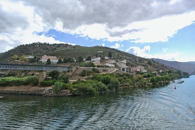 DC 22-0797-024.jpg :: Saga Douro River Cruise, Pocinho to Pinhao, River Douro: The Carrazeda de Ansiães railway bridge (also known as the Foz-Tua bridge) crossing the Douro River in Northern Portugal, a region known for its terraced vineyards. This striking iron truss bridge is located near the confluence of the Tua and Douro rivers in the municipality of Carrazeda de Ansiães. The bridge is situated in the heart of the Alto Douro region, which is a UNESCO World Heritage site known for its Port wine production. It is a railway bridge, part of the historical Douro railway line. The original structure was built in the late 19th or early 20th century, but a new bridge was constructed in 1980, featuring a mix of reinforced concrete for the access structures and a central metal truss. Photo taken 02/09/2022