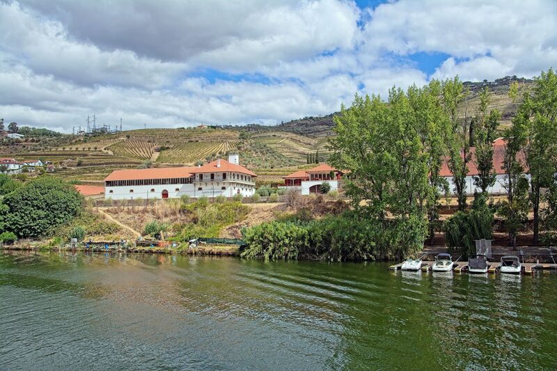 DC 22-0797-071.jpg :: Saga Douro River Cruise, Pocinho to Pinhao, River Douro: The village pictured in the image is Pinhão, a picturesque town nestled in the heart of Portugal's renowned Douro Valley wine region. The image shows the town from across the Douro River, featuring its distinctive iron bridge and the surrounding terraced hills covered in vineyards. Pinhão is located in the Norte Region of Portugal, within the Douro Valley, which is a UNESCO World Heritage site known for its stunning landscapes and port wine production. Photo taken 02/09/2022