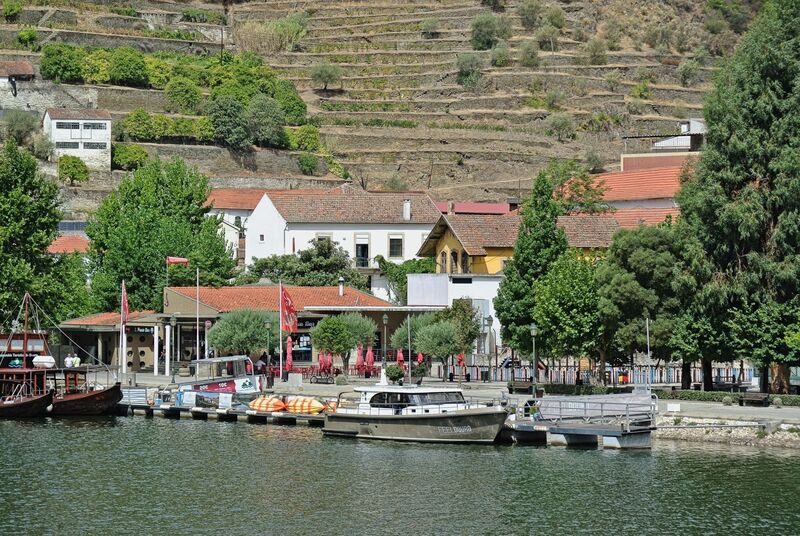 DC 22-0797-078.jpg :: Saga Douro River Cruise, Pocinho to Pinhao, River Douro: The village pictured in the image is Pinhão, a picturesque town nestled in the heart of Portugal's renowned Douro Valley wine region. The image shows the town from across the Douro River, featuring its distinctive iron bridge and the surrounding terraced hills covered in vineyards. Pinhão is located in the Norte Region of Portugal, within the Douro Valley, which is a UNESCO World Heritage site known for its stunning landscapes and port wine production. Photo taken 02/09/2022