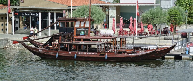 DC 22-0797-080.jpg :: Saga Douro River Cruise, Pocinho to Pinhao, River Douro: A traditional Portuguese rabelo boat docked in Pinhão, Portugal, likely used for tourist cruises on the Douro River. Rabelo boats traditionally transported barrels of Port wine from the Douro Valley vineyards to Vila Nova de Gaia. Modern versions, like the one pictured, are built for passengers and meet contemporary safety standards. These boats offer tours through the scenic, terraced vineyards of the UNESCO World Heritage region. Photo taken 02/09/2022