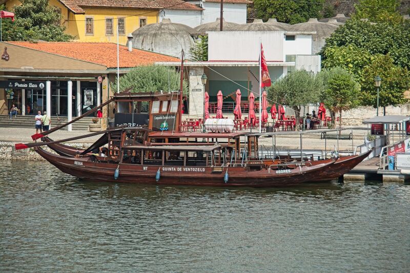 DC 22-0797-082.jpg :: Saga Douro River Cruise, Pocinho to Pinhao, River Douro: A traditional Portuguese rabelo boat docked in Pinhão, Portugal, likely used for tourist cruises on the Douro River. Rabelo boats traditionally transported barrels of Port wine from the Douro Valley vineyards to Vila Nova de Gaia. Modern versions, like the one pictured, are built for passengers and meet contemporary safety standards. These boats offer tours through the scenic, terraced vineyards of the UNESCO World Heritage region. Photo taken 02/09/2022