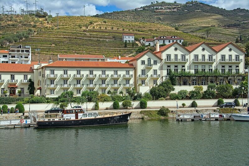 DC 22-0797-085.jpg :: Saga Douro River Cruise, Pocinho to Pinhao, River Douro: The village pictured in the image is Pinhão, a picturesque town nestled in the heart of Portugal's renowned Douro Valley wine region. The image shows the town from across the Douro River, featuring its distinctive iron bridge and the surrounding terraced hills covered in vineyards. Pinhão is located in the Norte Region of Portugal, within the Douro Valley, which is a UNESCO World Heritage site known for its stunning landscapes and port wine production. The vintage wooden yacht Friendship I. Photo taken 02/09/2022