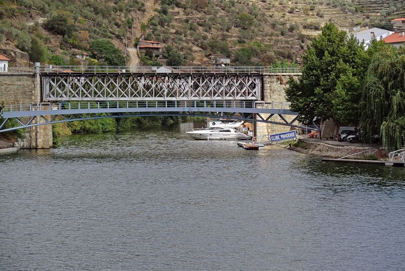 DC 22-0797-107.jpg :: Saga Douro River Cruise, Pocinho to Pinhao, River Douro: The Pinhão Railway Bridge, a prominent truss bridge that spans the Pinhão River at its confluence with the Douro River in Portugal. The structure is part of the historic Linha do Douro (Douro Line), which is renowned for its scenic views of the UNESCO-listed Douro Valley wine region. The bridge features a classic metal lattice truss design supported by robust stone masonry piers that extend into the water. It serves the Pinhão railway station, located nearby, which is famous for its traditional blue-and-white tile (azulejo) panels depicting the region's viticulture. Photo taken 02/09/2022