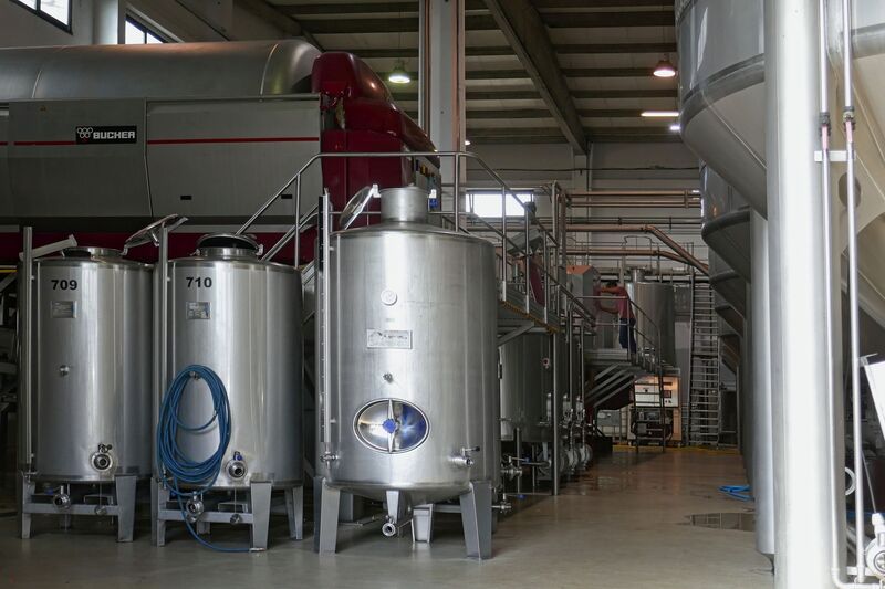 DC 22-0808-045.jpg :: Saga Douro River Cruise, Favaios:  The building in the image is the Adega Cooperativa de Favaios, a renowned winery located in the village of Favaios within the Douro wine region of Portugal. The winery is famous for producing one of Portugal's most iconic fortified wines, Moscatel de Favaios. The winery is nestled in the picturesque Alto Douro wine region of Portugal, a UNESCO World Heritage site. Founded in 1952, the cooperative was established by local producers to create their famous Moscatel wine. While most famous for its Moscatel, the winery also produces DOC Douro wines (white, red, and rosé), sparkling wines, and Port wine. Fermentation tanks. Photo taken 02/09/2022