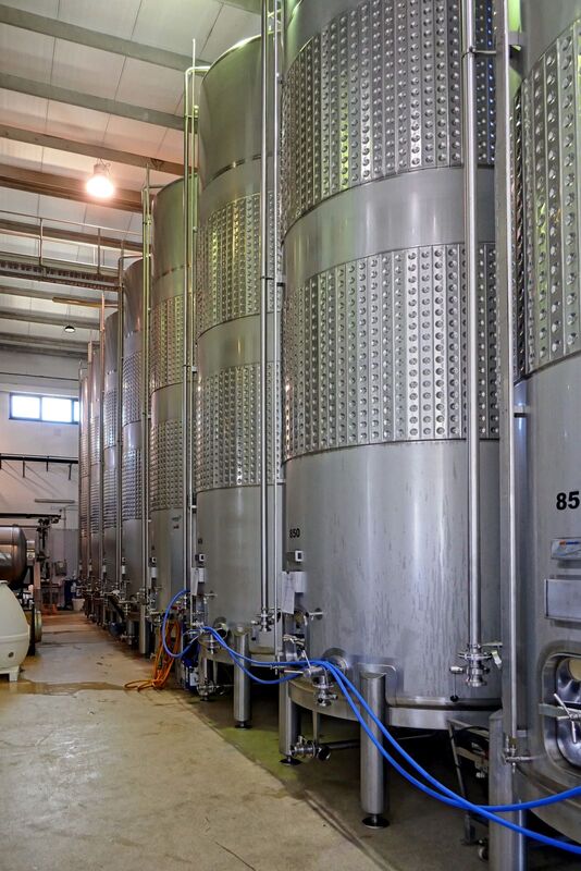 DC 22-0808-046.jpg :: Saga Douro River Cruise, Favaios:  The building in the image is the Adega Cooperativa de Favaios, a renowned winery located in the village of Favaios within the Douro wine region of Portugal. The winery is famous for producing one of Portugal's most iconic fortified wines, Moscatel de Favaios. The winery is nestled in the picturesque Alto Douro wine region of Portugal, a UNESCO World Heritage site. Founded in 1952, the cooperative was established by local producers to create their famous Moscatel wine. While most famous for its Moscatel, the winery also produces DOC Douro wines (white, red, and rosé), sparkling wines, and Port wine. Fermentation tanks. Photo taken 02/09/2022