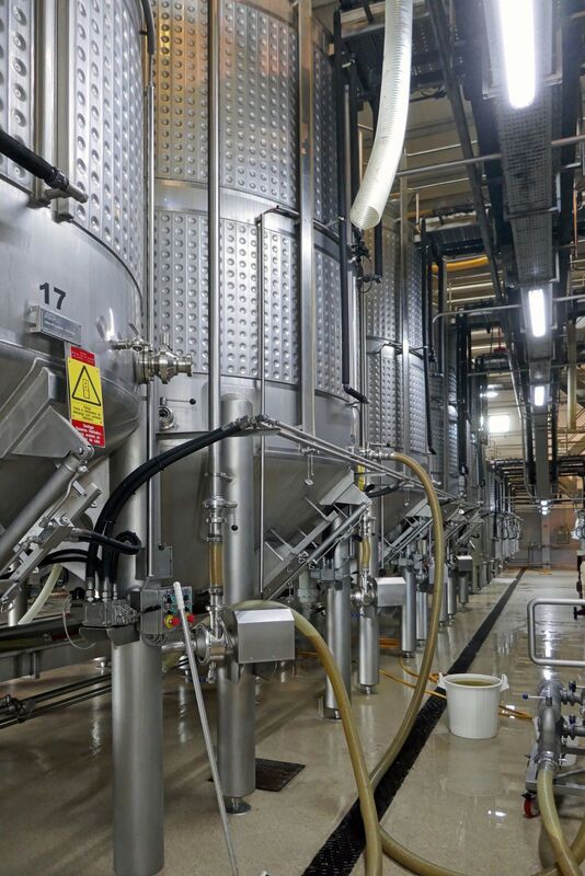 DC 22-0808-048.jpg :: Saga Douro River Cruise, Favaios:  The building in the image is the Adega Cooperativa de Favaios, a renowned winery located in the village of Favaios within the Douro wine region of Portugal. The winery is famous for producing one of Portugal's most iconic fortified wines, Moscatel de Favaios. The winery is nestled in the picturesque Alto Douro wine region of Portugal, a UNESCO World Heritage site. Founded in 1952, the cooperative was established by local producers to create their famous Moscatel wine. While most famous for its Moscatel, the winery also produces DOC Douro wines (white, red, and rosé), sparkling wines, and Port wine. Fermentation tanks. Photo taken 02/09/2022