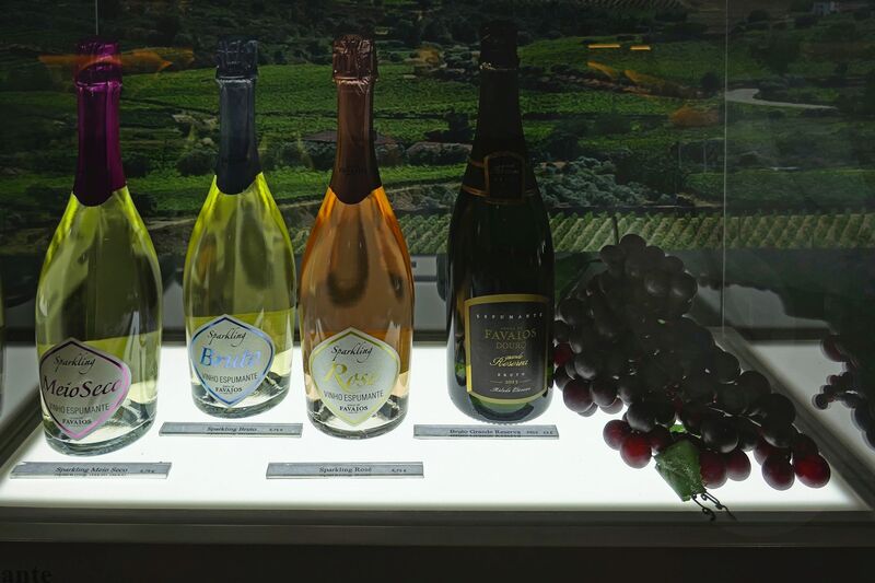 DC 22-0808-060.jpg :: Saga Douro River Cruise, Favaios:  The building in the image is the Adega Cooperativa de Favaios, a renowned winery located in the village of Favaios within the Douro wine region of Portugal. The winery is famous for producing one of Portugal's most iconic fortified wines, Moscatel de Favaios. The winery is nestled in the picturesque Alto Douro wine region of Portugal, a UNESCO World Heritage site. Founded in 1952, the cooperative was established by local producers to create their famous Moscatel wine. While most famous for its Moscatel, the winery also produces DOC Douro wines (white, red, and rosé), sparkling wines, and Port wine. Local wine producers bringing their grapes for quality checking and unloading. Vinho Espumante Wines available for purchase. Photo taken 02/09/2022