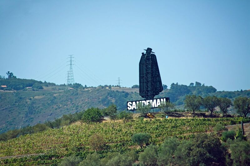 DC 22-0809-003.jpg :: Saga Douro River Cruise, Pinhao to Regua, Portugal: The iconic Don Sandeman logo overlooking terraced vineyards in the Douro Valley, Portugal. This large-scale silhouette is a famous landmark in the region, specifically near the town of Peso da Régua. The \