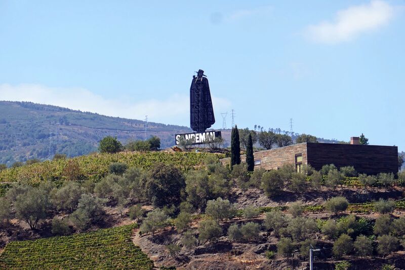 DC 22-0809-010.jpg :: Saga Douro River Cruise, Pinhao to Regua, Portugal: The iconic Don Sandeman logo overlooking terraced vineyards in the Douro Valley, Portugal. This large-scale silhouette is a famous landmark in the region, specifically near the town of Peso da Régua. The \