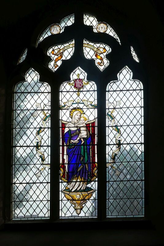 DC 24-0736-033.jpg :: Tenterden, Kent: St. Mildred's Church is an Anglican church located in Tenterden in the borough of Ashford in Kent. The church dates from about the 12th century and is Grade I heritage listed. The main tower of the church is 39.6 metres (130 feet) high and was constructed in 1461. It is dedicated to a prominent Anglo-Saxon saint, Saint Mildred, a 7th-century princess who served as the abbess of the nunnery at Minister-in-Thanet. The main tower of the church is built from Bethersden Marble, a limestone that contains thousands of brightly coloured shells. A graveyard is also present on the left-hand side of the church. Stained glass window. Madonna & Child - Christopher Webb of St Albans 1931. Photo taken 04/09/2024