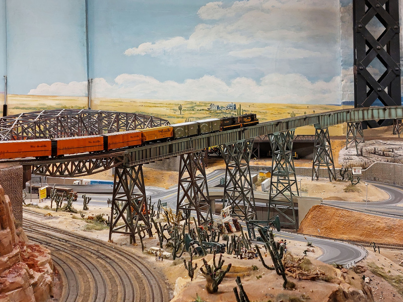 DC 25-0767-080.jpg :: Miniatur Wunderland Hamburg, Germany: The Miniatur Wunderland is, according to Guinness World Records, the largest model railway system in the world. It is located at the historic Speicherstadt in Hamburg and is one of the most popular and most visited sights in Germany. The exhibition includes around 1,230 digitally controlled trains with more than 12,000 wagons. The Wonderland is also designed with around 4,300 houses and bridges, more than 10,000 vehicles – of which around 350 drive independently on the installation – 47 airplanes and around 290,000 figures. The system features a recurring day-night lighting cycle and almost 500,000 built-in LED lights. Of the 7,000 m2 (75,347 sq ft) of floorspace, the models occupy 1,545 m2 (16,630 sq ft). P.s. Part of the USA section of the exhibition. Rail track passing over desert terrain. Photo taken 20/01/2025