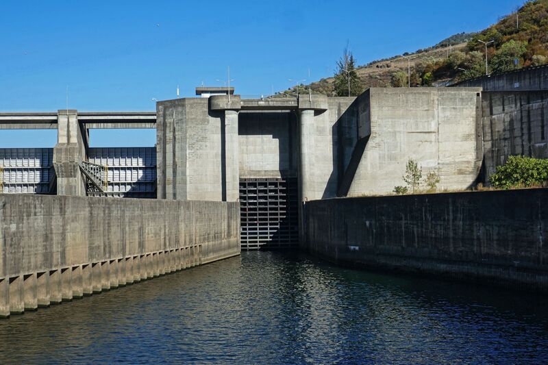 DC 22-0789-032.jpg :: Saga Douro River Cruise, Regua Lamego to Pinhao, River Douro: Régua Dam (Portuguese: Barragem da Régua) is a concrete gravity dam on the Douro, where the river forms the border line between the districts of Vila Real and Viseu. It is located in the municipality Peso da Régua, in Vila Real District. Construction of the dam began in 1965. The dam was completed in 1973. It is owned by Companhia Portuguesa de Produção de Electricidade (CPPE). Photo taken 30/08/2022.