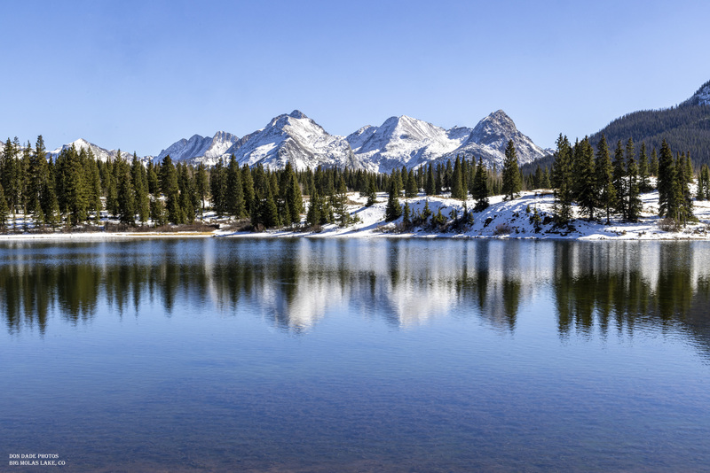 Big Molas Lake Colorado.jpg :: Big Molas Lake is located at the summit between Durango and Silverton Colorado at 10,508 feet in elevation.

I am drawn to snowcapped mountains.  Especially with a clear calm lake water at my feet.
I stood gazing at the moss-covered bottom of the lake, interrupted by the rings of fish breaking the surface of the water.
Then taking notice of the reflections of the surrounding forest and distant mountain peaks of Mt Garfield, Graystone and Electric Peak.
The casting of the early afternoon shadows moving slowly across the snow-covered ground.
The whole scene accented by the clear pale blue sky.  So grateful for the opportunity to take in the beauty and awe of this surreal scenery.
As I sit here now, I take pause in the memory of breathing in the clean crisp fresh air of this peaceful mountain summit lake, this image forever engraved in my mind.
