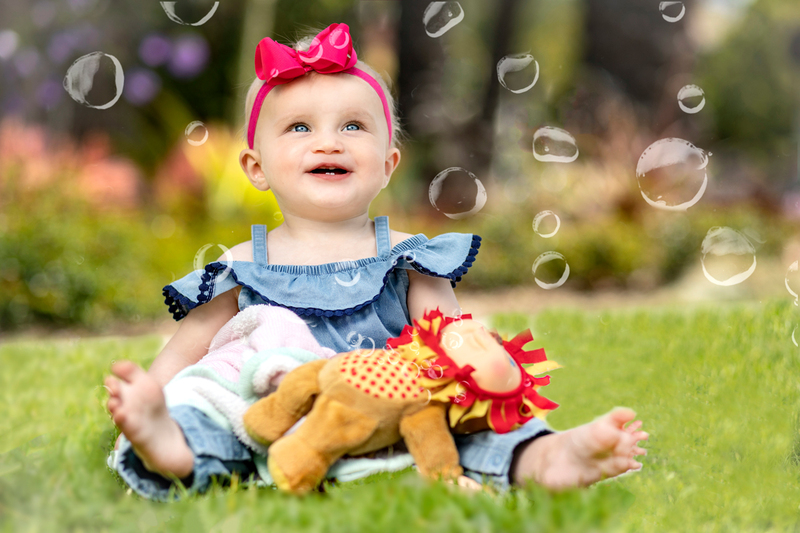 Baby Girl in pink bow smiling at bubbles while sitting in grass at a park.jpg :: Baby Girl in pink bow smiling at bubbles while sitting in grass at a park