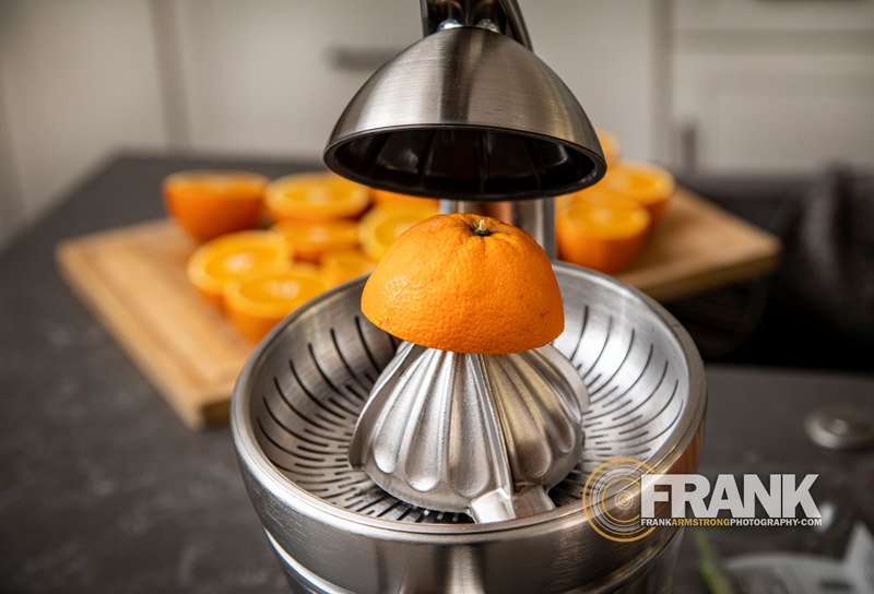 Orange juicer with sliced oranges in the background  001LOGO.jpg :: Horizontal image of half an orange in a juicer with oranges in the background