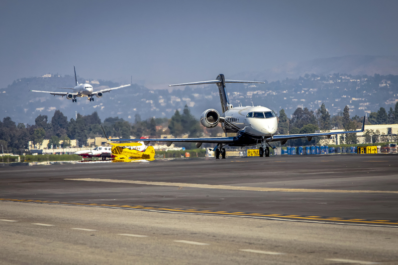 Private Jet taxiing with commercial Jet landing in background002.jpg :: Private jet taxiing with heat from engines visible. Commercial jet diffused landing in distance.