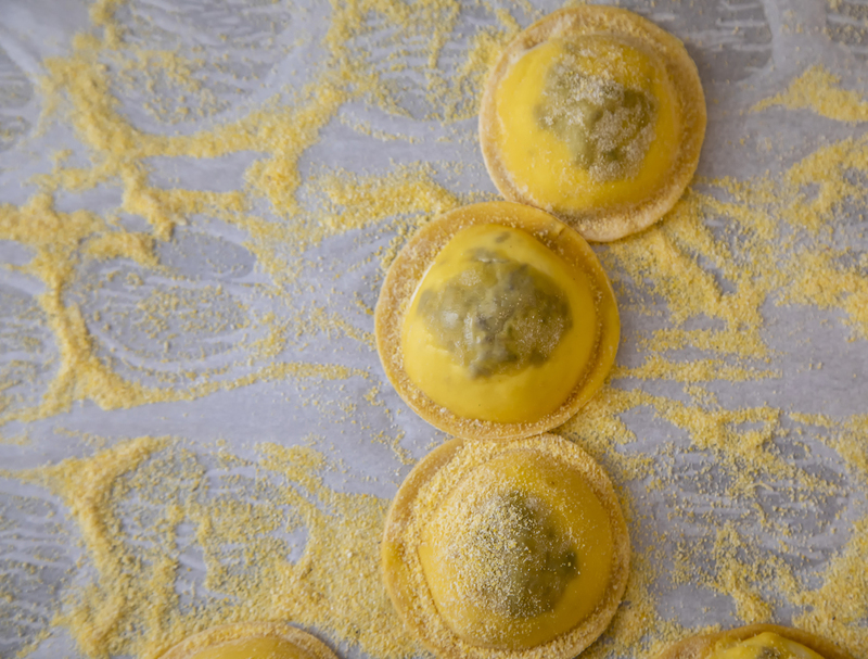 Ravolinis stuffed with sausage and dusted with semilina flour 1.jpg :: Horizontal and top view of Raviolis uncooked stuffed with sausage and mushrooms uncooked on wax paper on a baking sheet