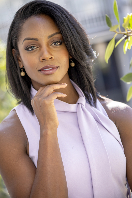 African American woman in pink dress001(1).jpg :: Tight shot of African American woman in pink dress looking straight into camera with leaves and building diffused in background