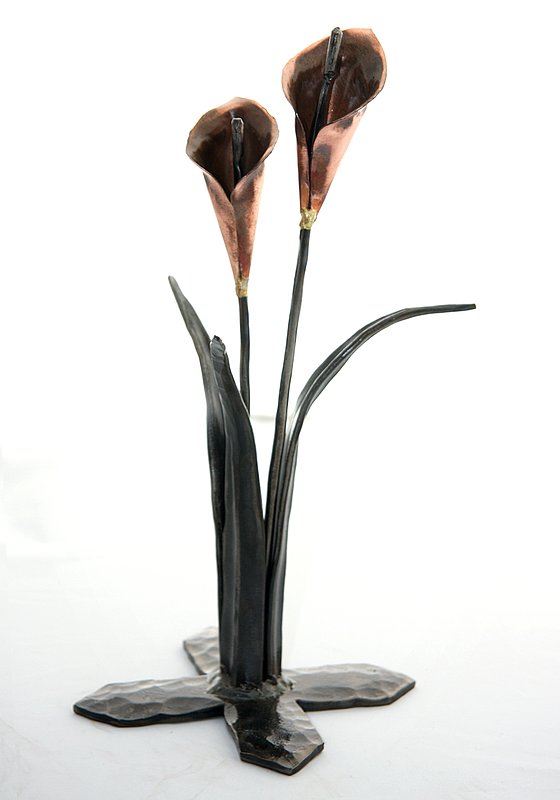 Calla Lillies - Front.jpg :: $75.00 - The design of these calla lilies shows off the beauty of hand-forged metal. Hammer marks add texture to the base, and the leaves seem to open as delicately as anything in nature. The lilies themselves are shaped from copper sheeting that is formed, fitted, and even fluted at the ends. The stems are made from metal rods which rise through the flower and whose ends have been rounded to look like a stamen. The base of this piece is approx 4\