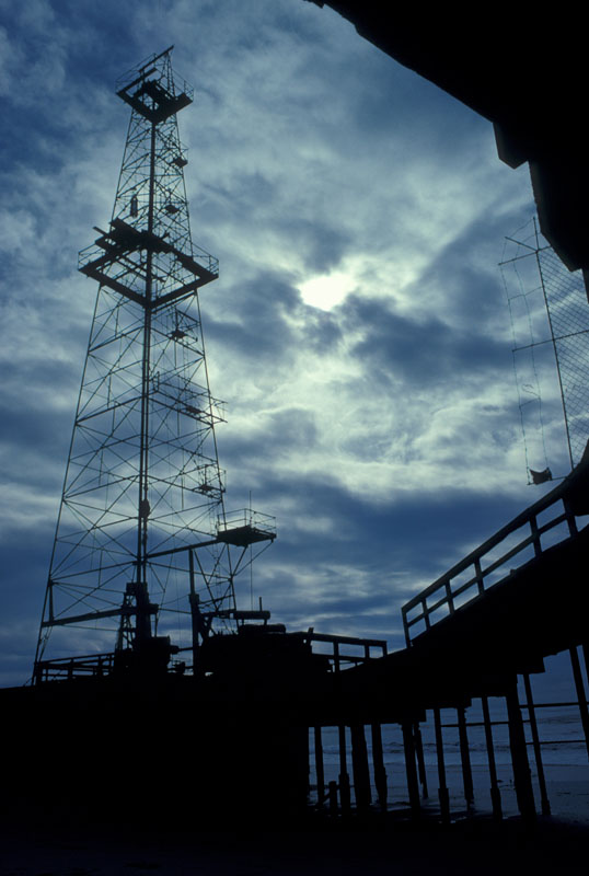 Oil Derrick.jpg :: This oil derrick was off the Calif coast near Santa Barbara. The leading lines of the dock lead the viewers eye right to the subject and the dramatic lighting doesn't hurt either. This was shot on 35mm transparency film in 1979 and digitized in 2006. Still good quality.