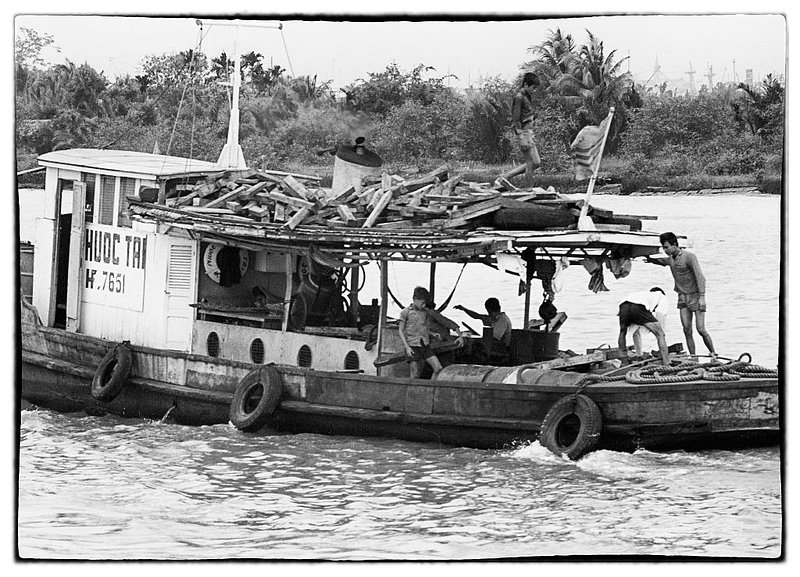 House Boat.jpg :: The Mekong Delta has long-lasting agricultural traditions. Slow-moving waterways are alive with shrimp and river fish, while all year round, the fertile soil yields an abundant crop of fruit, rice, and vegetables. During my time on the rivers children waded out toward our barges expecting Rations to be thrown to them by Soldiers. All of the river ways were hot beds  with fire put forth from the banks of the jungle.. Navagation of waters during daylight was staying in the middle. Barges carried 105 and 155 Howitzers and were fully operational.