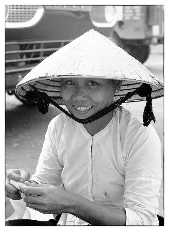 Vietnamese Woman.jpg :: Captured this street portrait of a young Vietnamese woman sitting along a roadside. I noticed that she had spotted me photographing and catching her attention I approached and caught her smiling face. Most Vietnamese appear to be friendly and enjoy attention especially from Americans. In conversations they are inquisitive about the United States, family life here and geography.