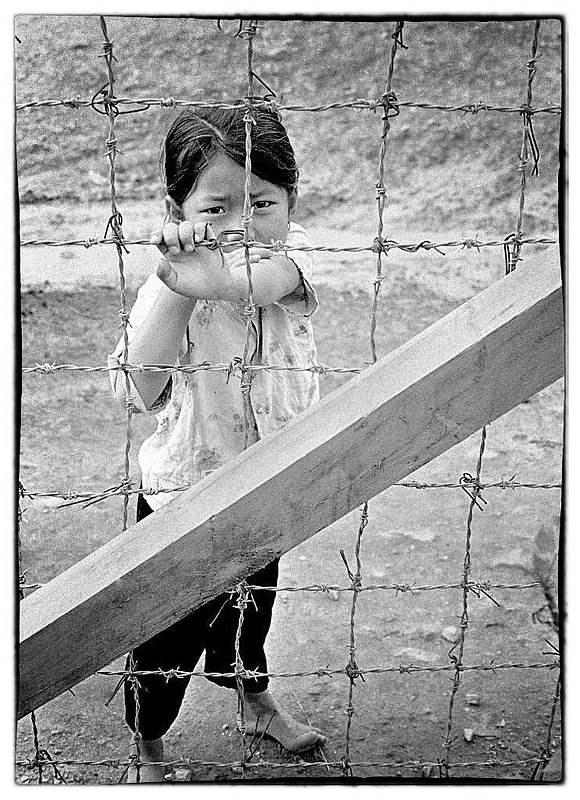 War and Child.jpg :: Many of the children that approach fenced areas have a look of sadness coupled with curiosity as to what is going on, i'm sure that in their world they do not understand. Often times they are hungry and begging for food or a few dong to buy street food.