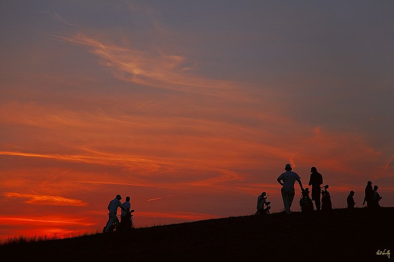 E101--Caddies  01  V1  1500px  with signature  SS.jpg :: Players and their caddies on the 18th green silhouetted against a late evening sky at Erin Hills, a daily fee golf course in Erin, Wisconsin.  Erin Hills was designed by Hurdzan/Fry and Ron Whitten and built by Landscapes Unlimited, LLC, and has been choosen to host the 2011 US Amateur Chanpionship and the 2017 US Open Championship.  Photo by Paul Hundley; taken in September, 2012.