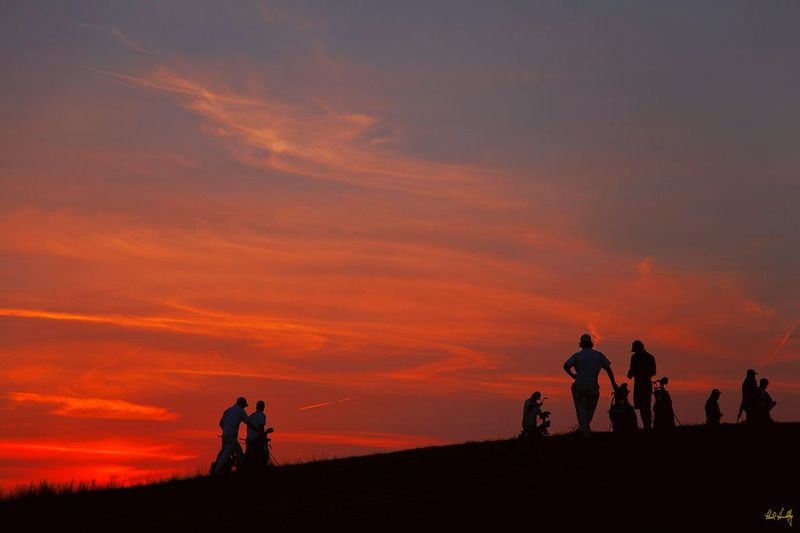 E101--Caddies  01  V1  1500px  with signature  SS1.jpg :: Players and their caddies on the 18th green silhouetted against a late evening sky at Erin Hills, a daily fee golf course in Erin, Wisconsin.  Erin Hills was designed by Hurdzan/Fry and Ron Whitten and built by Landscapes Unlimited, LLC, and has been choosen to host the 2011 US Amateur Chanpionship and the 2017 US Open Championship.  Photo by Paul Hundley; taken in September, 2012.