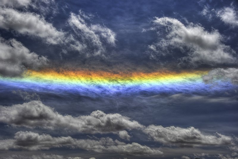 GBL-UTM-18.jpg :: A circumhorizontal arc, also known as a fire rainbow, is an optical phenomenon that belongs to the family of ice halos formed by the refraction of sun- or moonlight in plate-shaped ice crystals suspended in the atmosphere, typically in cirrus or cirrostratus clouds. In its full form, the arc has the appearance of a large, brightly spectrum-coloured band (red being the topmost colour) running parallel to the horizon, located far below the Sun or Moon. The distance between the arc and the Sun or Moon is twice as far as the common 22-degree halo. Often, when the halo-forming cloud is small or patchy, only fragments of the arc are seen. As with all halos, it can be caused by the Sun as well as (but much more rarely) the Moon. Other currently accepted names for the circumhorizontal arc are circumhorizon arc or lower symmetric 46 degree plate arc. The misleading term \